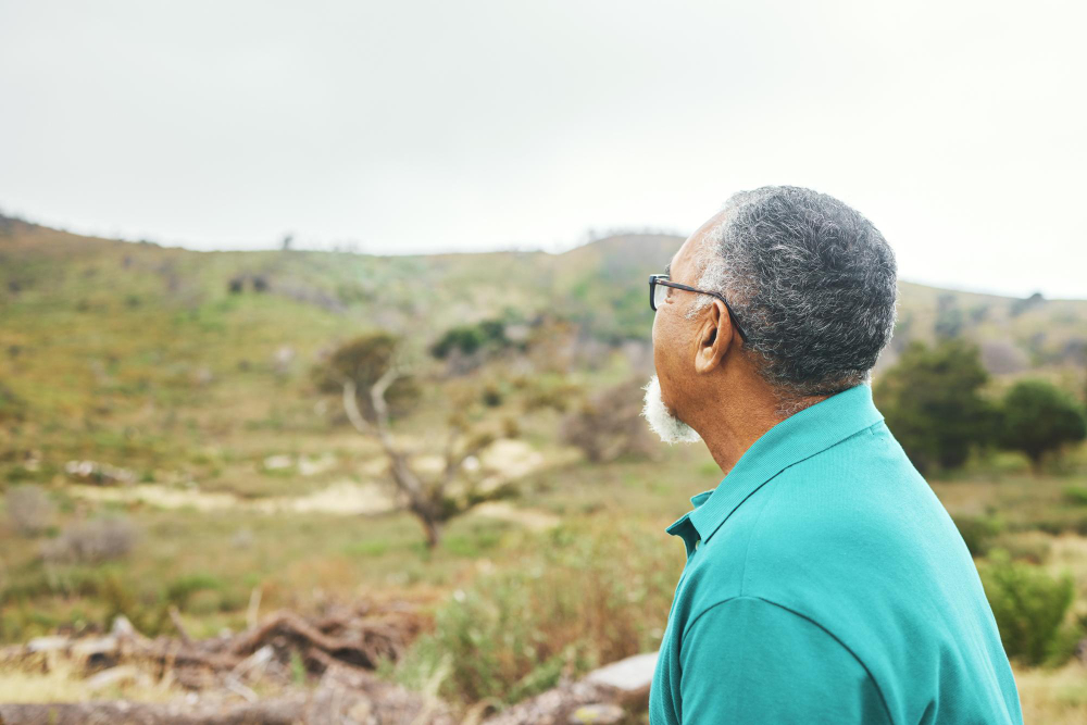 Idoso observa uma paisagem natural com vegetação e colinas ao ar livre.