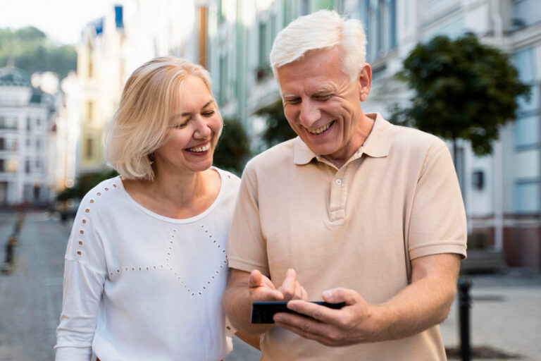 Casal maduro ao ar livre em uma rua urbana, sorrindo enquanto olham juntos para a tela de um celular.